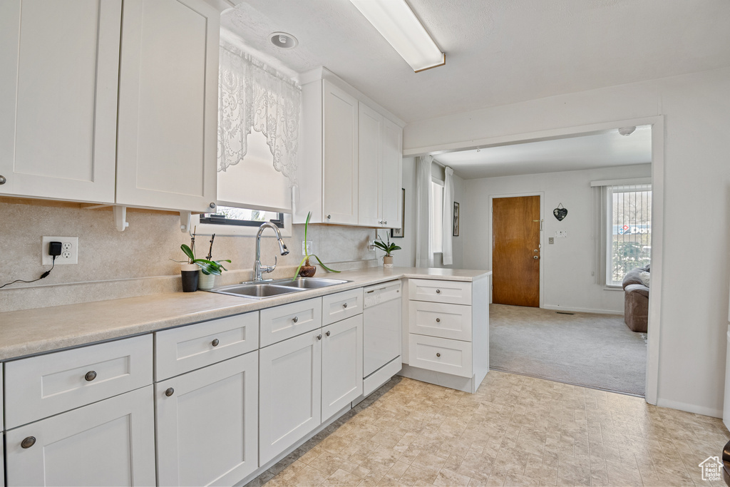 Kitchen with a sink, white dishwasher, white cabinets, and light countertops