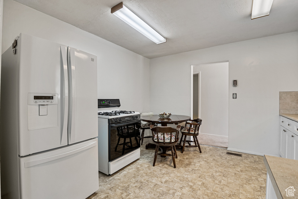 Kitchen with white refrigerator with ice dispenser, range with gas cooktop, light countertops, and white cabinetry