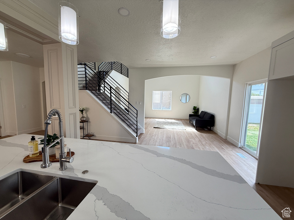 Kitchen featuring a sink, a textured ceiling, wood finished floors, light stone countertops, and arched walkways