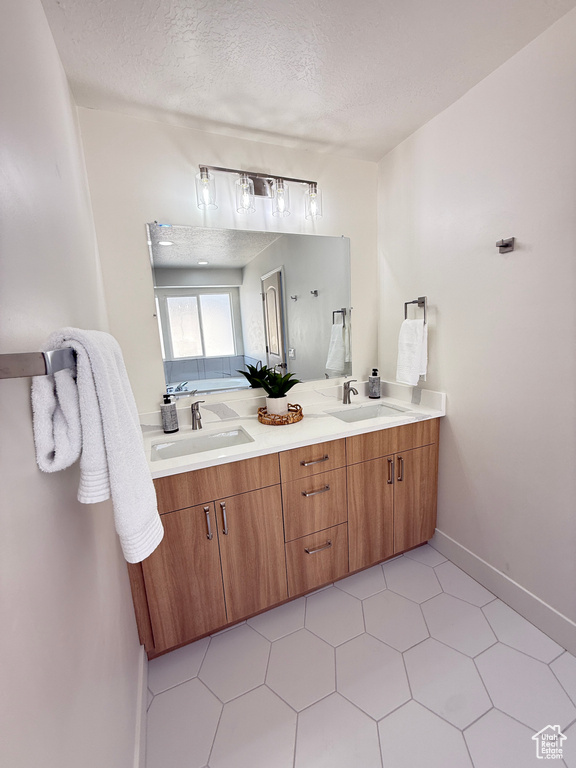 Bathroom featuring double vanity, a textured ceiling, and baseboards