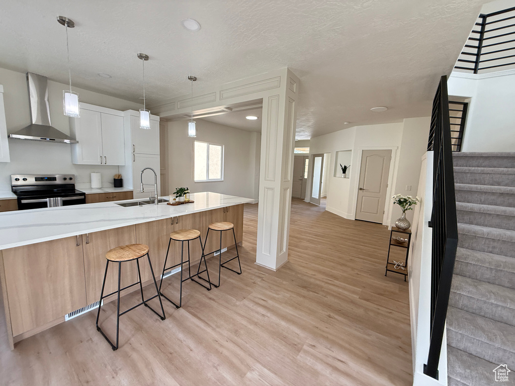Kitchen featuring wall chimney range hood, stainless steel range with electric cooktop, a sink, and light wood-type flooring