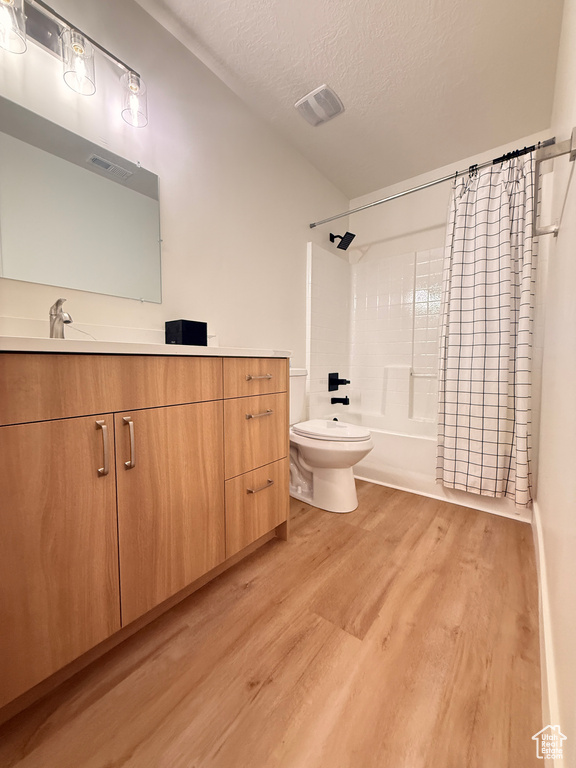 Full bath with wood finished floors, a textured ceiling, tub / shower combination, toilet, and vanity