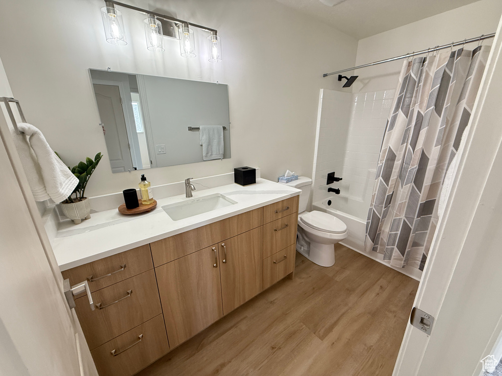 Bathroom featuring toilet, vanity, wood finished floors, and shower / bathtub combination with curtain