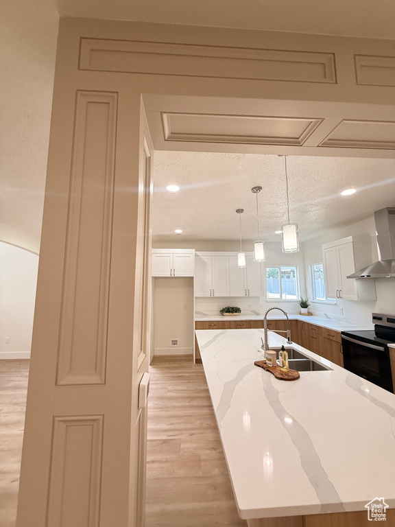 Kitchen featuring wall chimney range hood, electric range, a sink, light wood-style floors, and white cabinetry