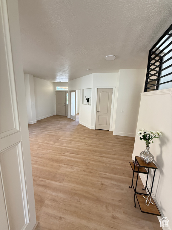 Unfurnished living room featuring a textured ceiling, baseboards, and light wood-type flooring