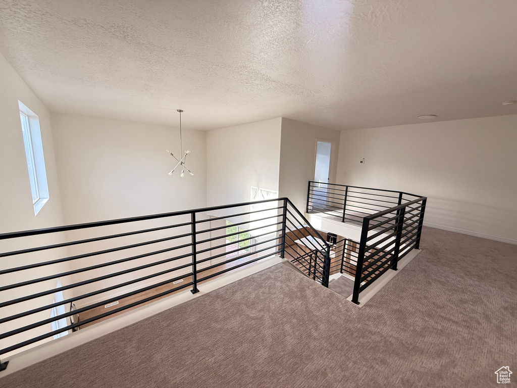 Hallway featuring an upstairs landing, a textured ceiling, carpet flooring, a chandelier, and baseboards