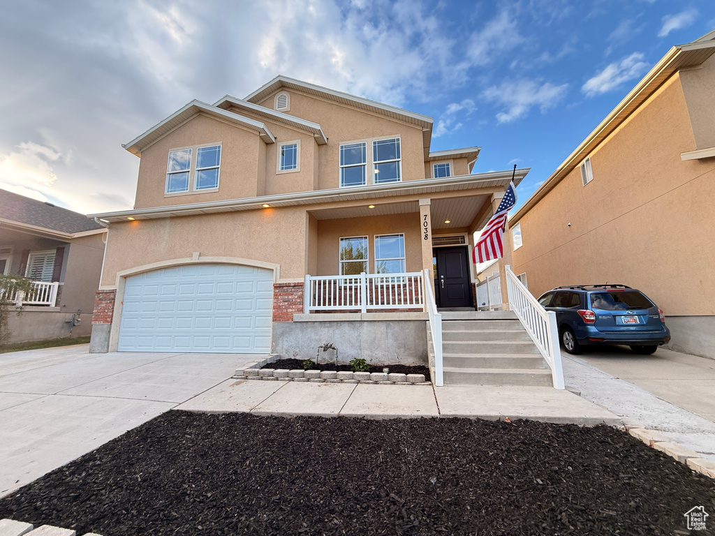View of front of home with covered porch, an attached garage, concrete driveway, and stucco siding
