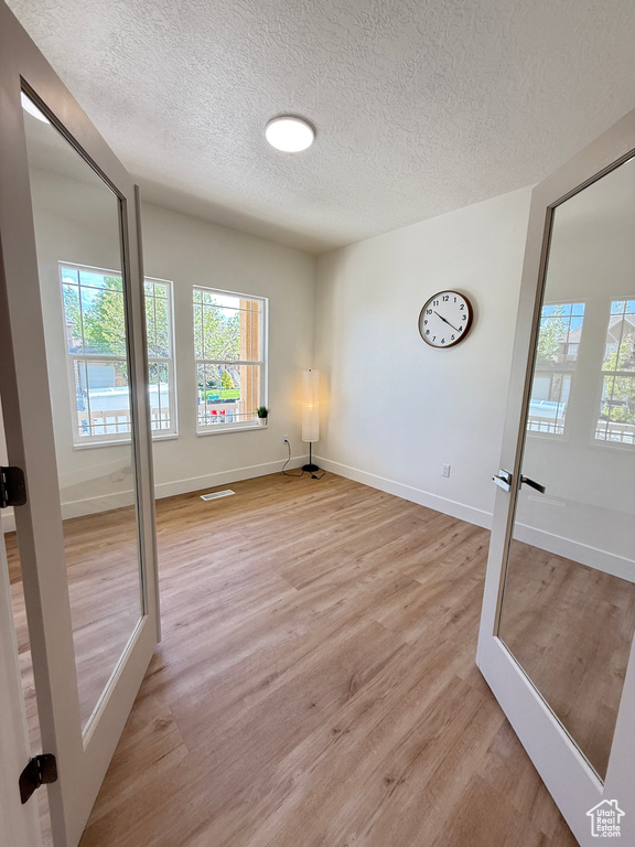 Unfurnished room with a textured ceiling, light wood-style flooring, healthy amount of natural light, and baseboards