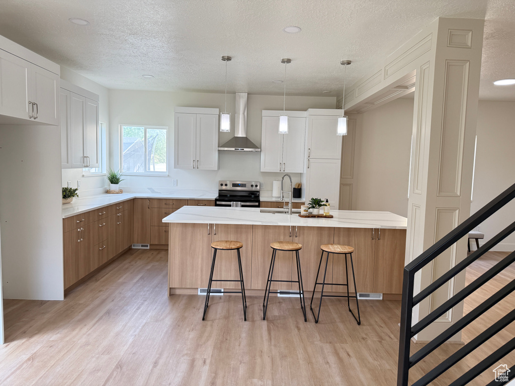 Kitchen featuring wall chimney range hood, stainless steel electric range oven, light wood-type flooring, a sink, and a textured ceiling