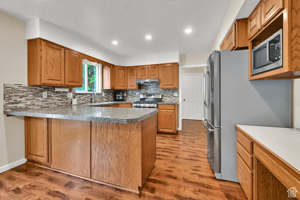 Kitchen with stainless steel appliances, under cabinet range hood, wood finished floors, backsplash, and a peninsula