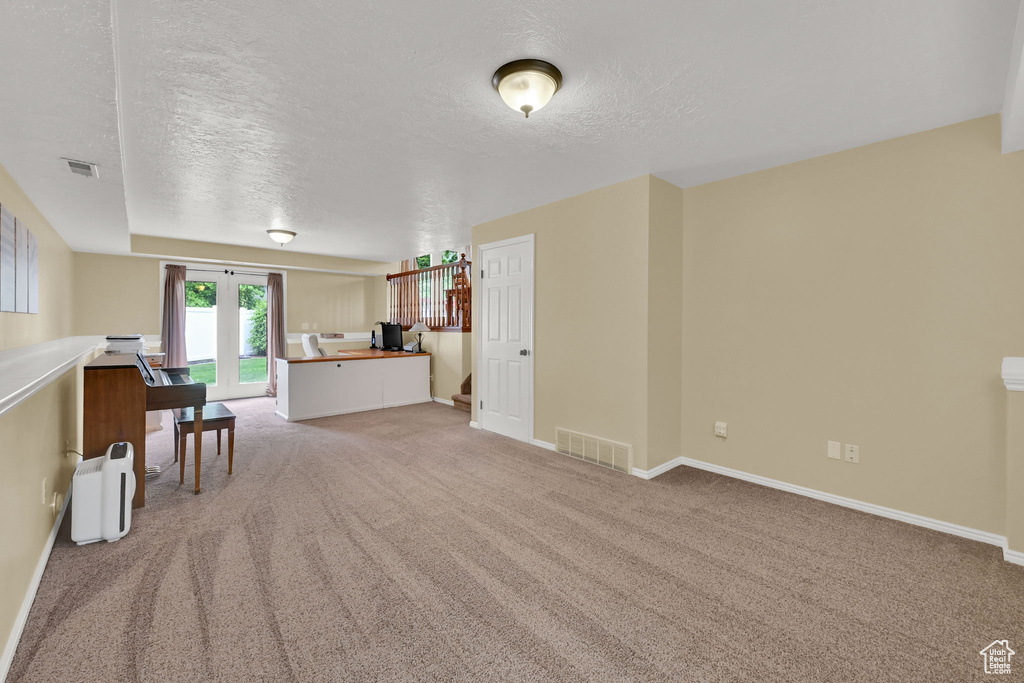 Living room with a textured ceiling, light carpet, an office area, and baseboards