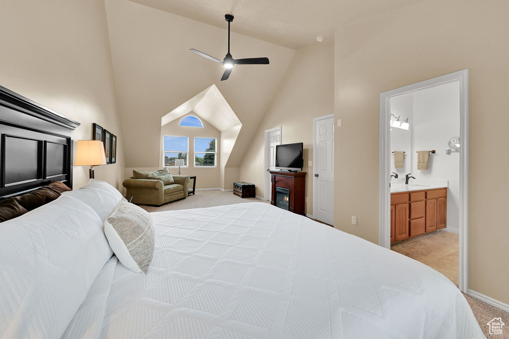 Bedroom with vaulted ceiling, light carpet, baseboards, connected bathroom, and a sink