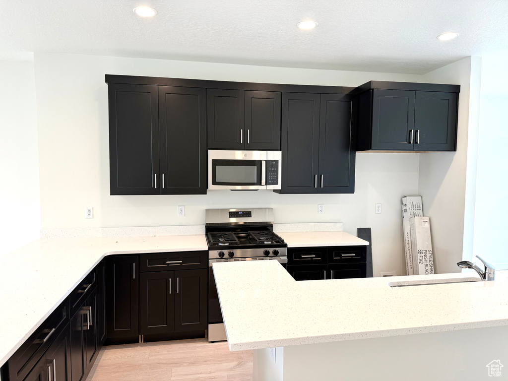 Kitchen with appliances with stainless steel finishes, a sink, dark cabinets, light stone counters, and recessed lighting