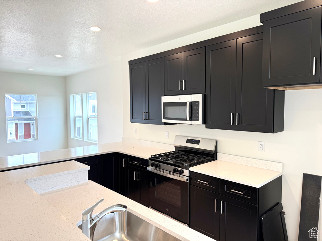 Kitchen featuring stainless steel appliances, dark cabinets, recessed lighting, a textured ceiling, and light stone counters