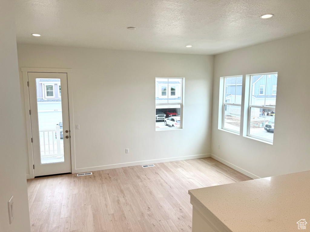 Unfurnished dining area with light wood-style floors, recessed lighting, baseboards, and a textured ceiling
