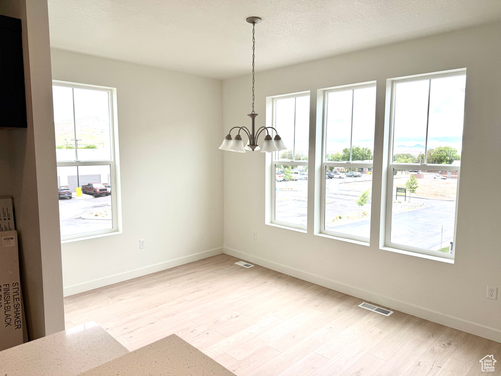 Unfurnished dining area with plenty of natural light, light wood finished floors, and a chandelier