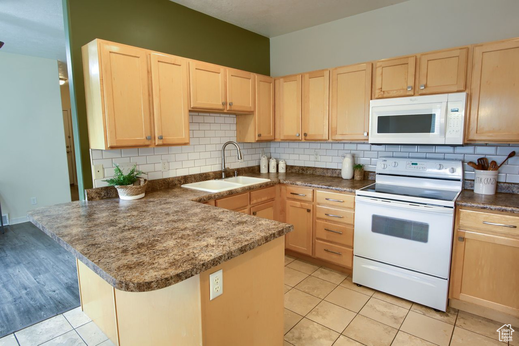 Kitchen featuring white appliances, light brown cabinetry, a sink, a peninsula, and backsplash