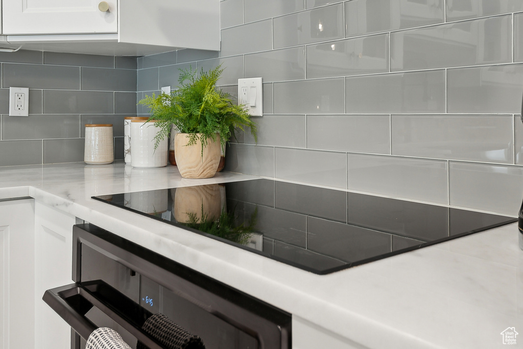 Kitchen view of tasteful backsplash, white cabinetry, light countertops, and wall oven