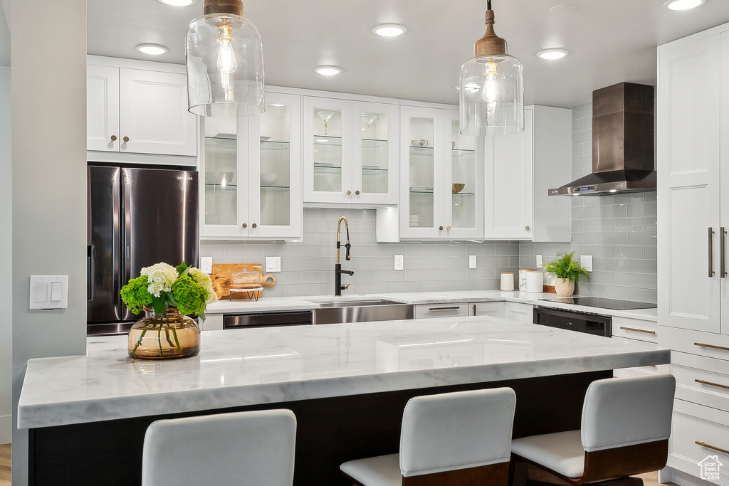 Kitchen with wall chimney exhaust hood, freestanding refrigerator, a sink, a kitchen bar, and recessed lighting