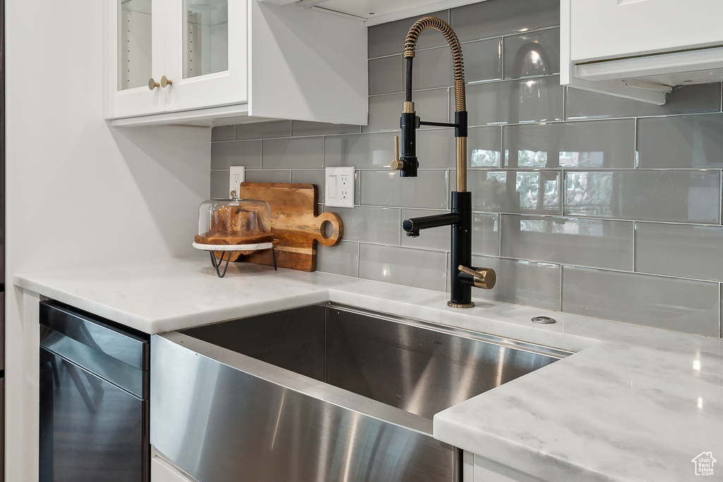 Kitchen view of backsplash, white cabinetry, glass insert cabinets, light stone counters, and a sink