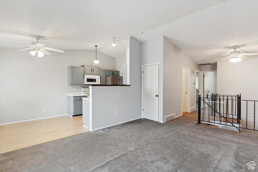 Unfurnished living room featuring a ceiling fan, lofted ceiling, baseboards, and light colored carpet