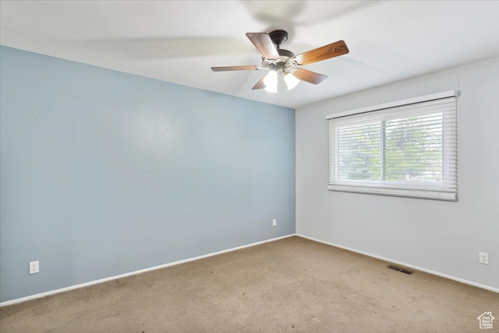 Carpeted spare room featuring ceiling fan and baseboards