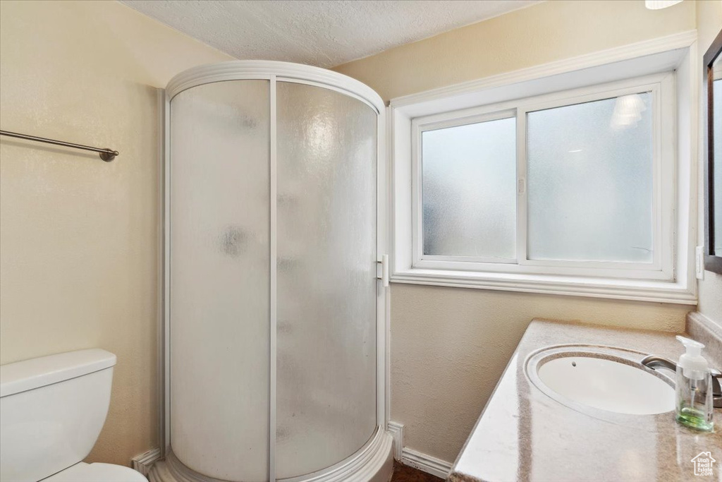 Full bathroom featuring a stall shower, toilet, a sink, and a textured ceiling