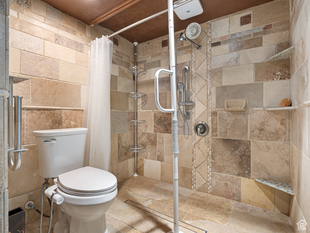 Bathroom with a tile shower, toilet, and stone tile flooring
