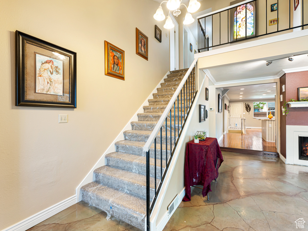 Stairway with crown molding, a lit fireplace, baseboards, and a chandelier