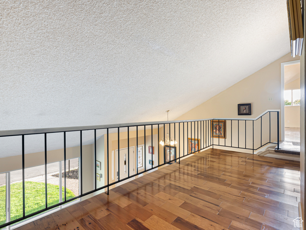 Corridor featuring a textured ceiling, hardwood / wood-style floors, and lofted ceiling