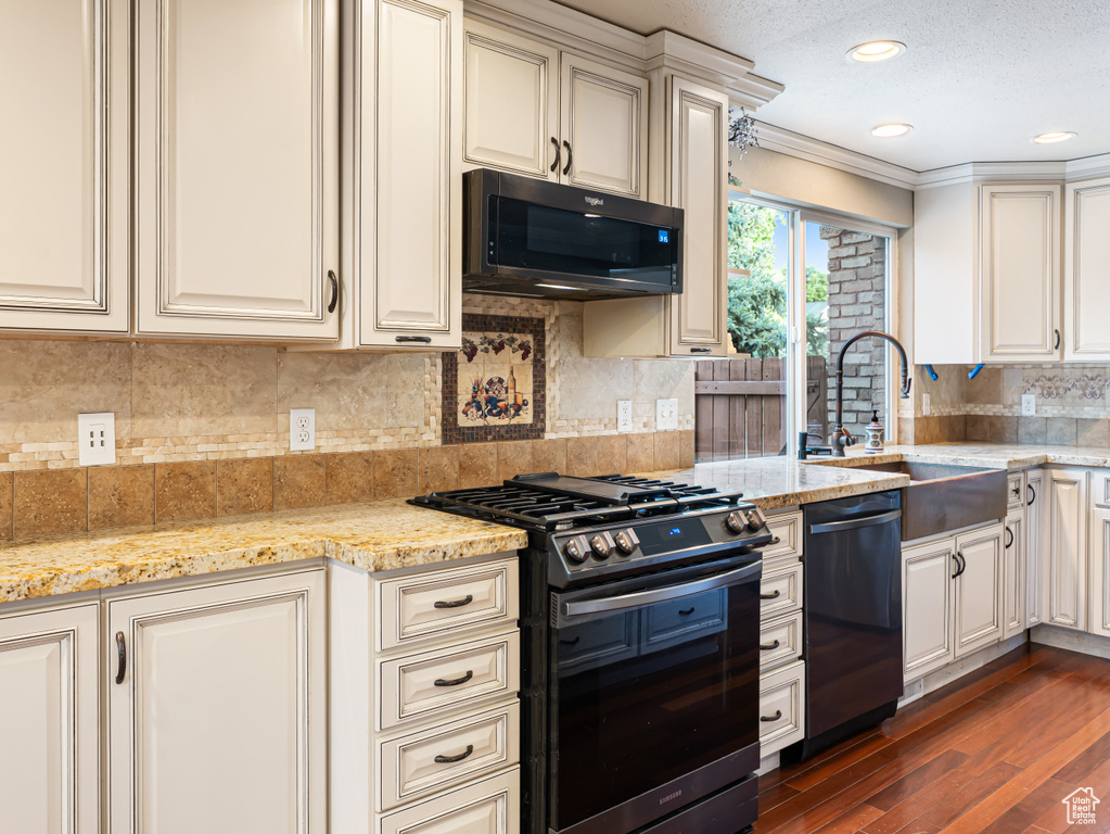 Kitchen featuring stainless steel gas stove, dishwasher, a sink, dark wood-style floors, and cream cabinetry