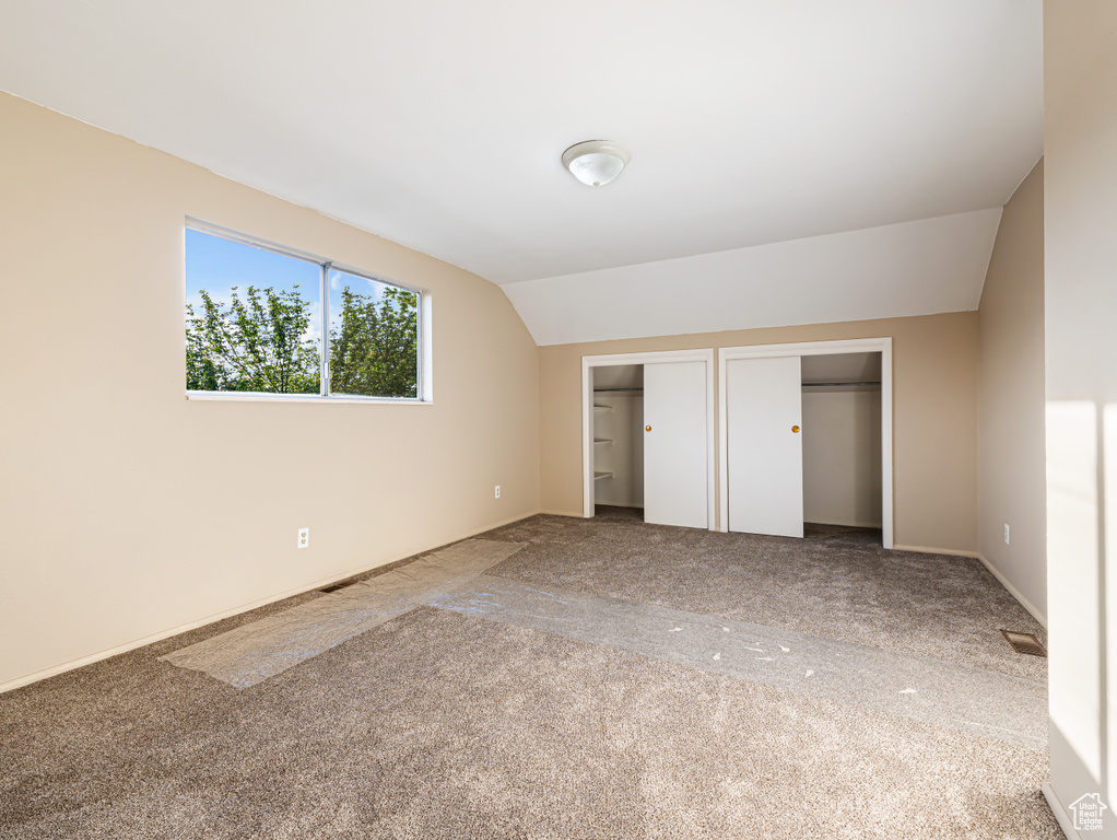 Unfurnished bedroom with multiple closets, lofted ceiling, and carpet flooring