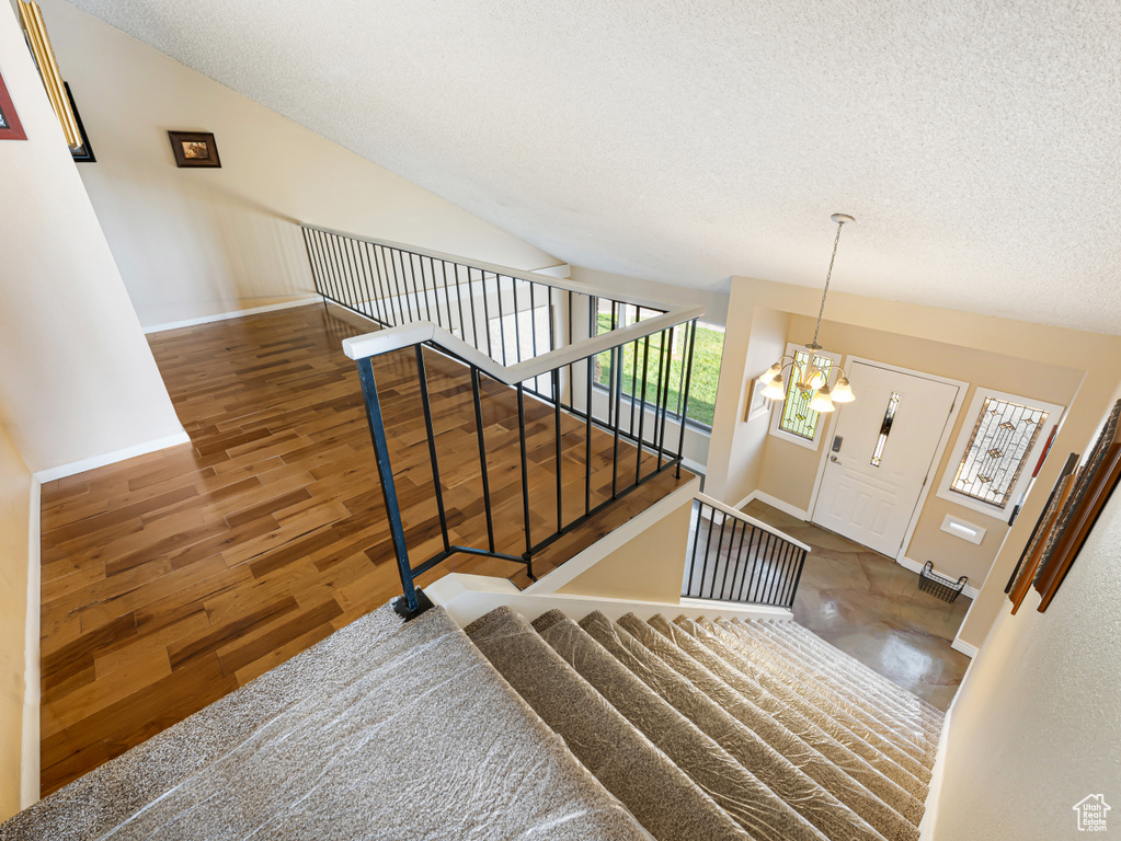 Stairs featuring a textured ceiling, baseboards, a chandelier, and wood finished floors