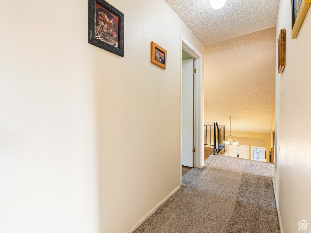 Corridor featuring carpet, a textured ceiling, a chandelier, and baseboards