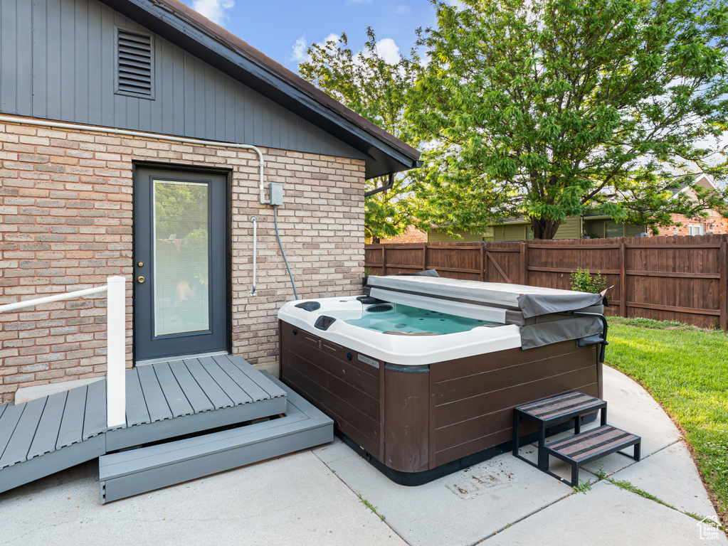 Wooden terrace with a hot tub, fence, and a patio area