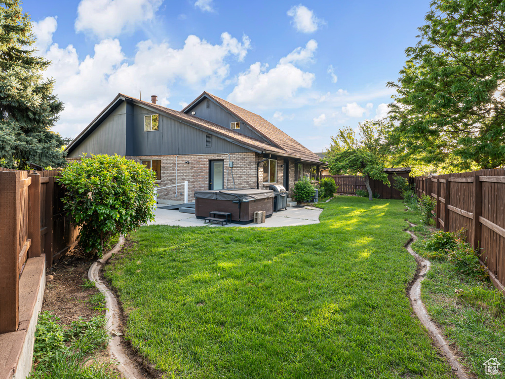 Rear view of property with a hot tub, brick siding, and a patio area