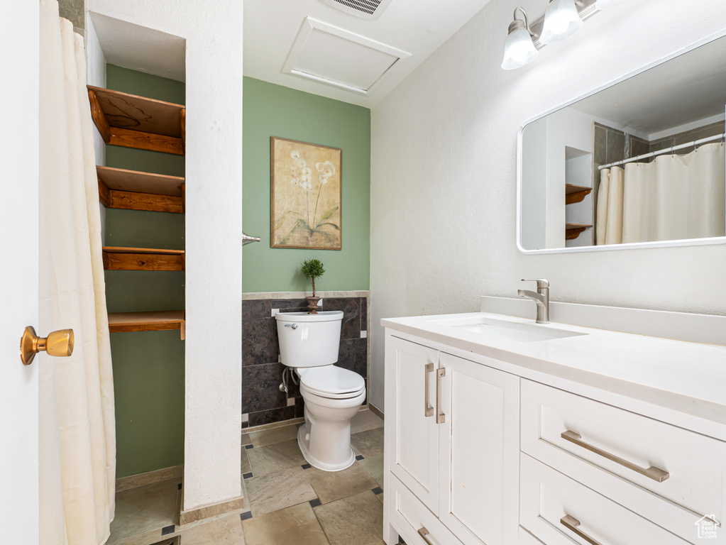 Bathroom with toilet, vanity, tile walls, and a wainscoted wall