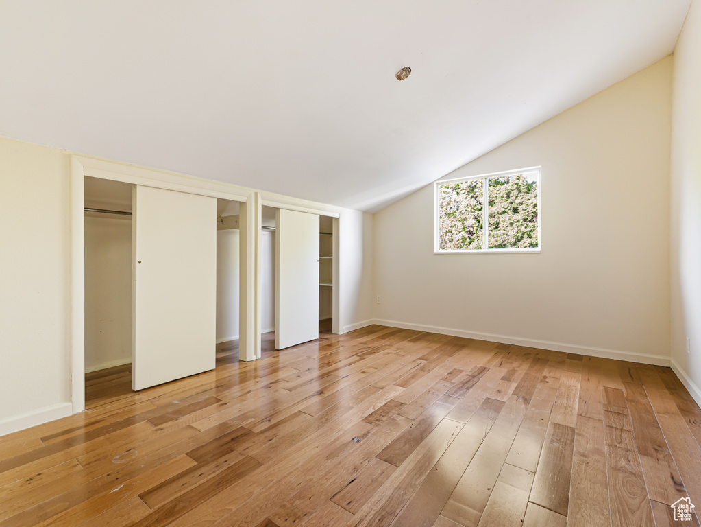 Unfurnished bedroom featuring multiple closets, light wood-style floors, lofted ceiling, and baseboards
