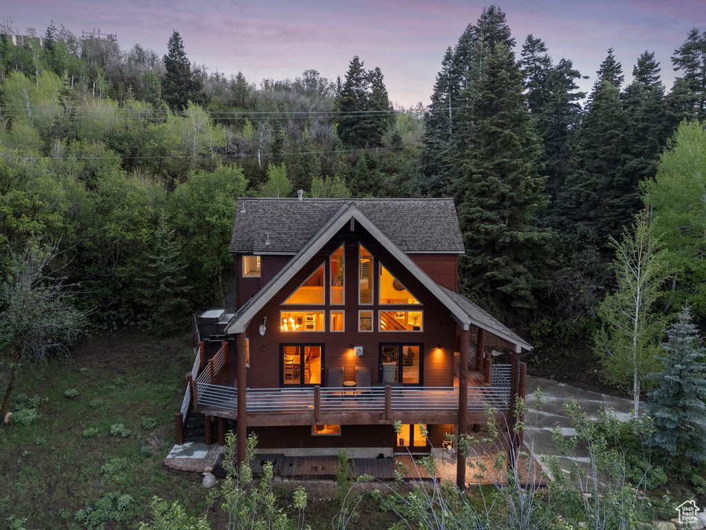 Back of house with a view of trees and a shingled roof