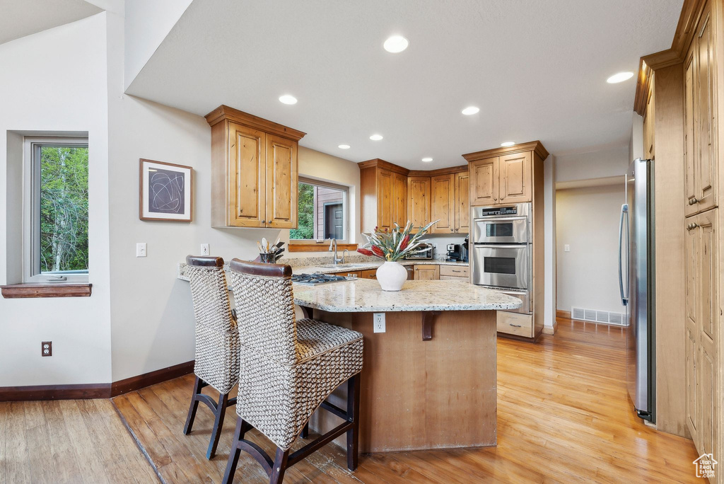 Kitchen with stainless steel appliances, a warming drawer, baseboards, a kitchen bar, and plenty of natural light