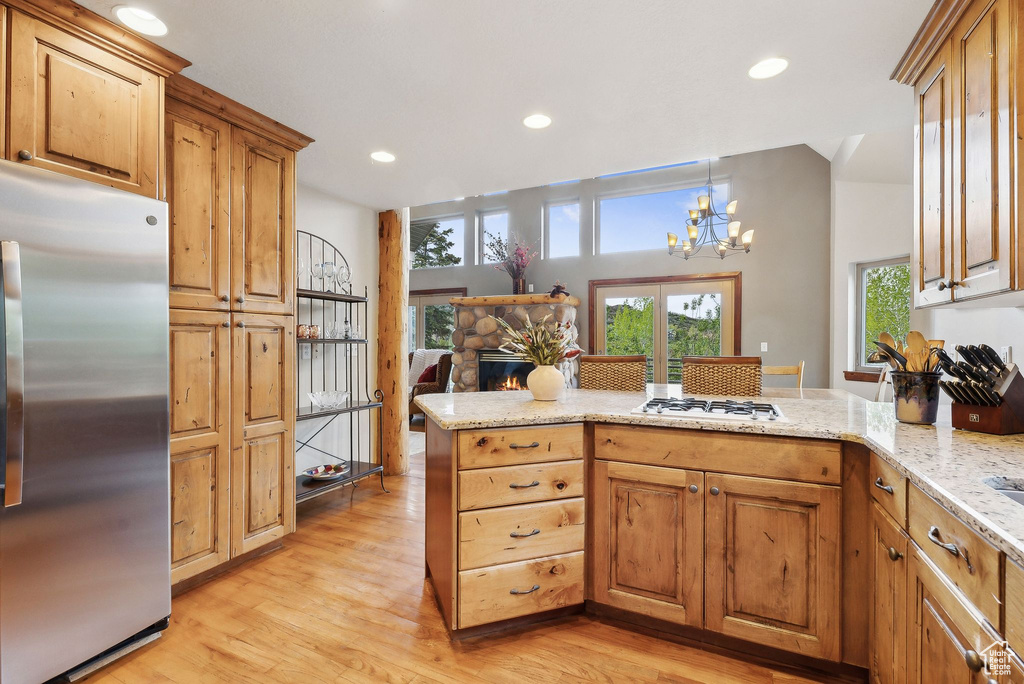 Kitchen with stainless steel refrigerator, a peninsula, light wood-type flooring, light stone countertops, and recessed lighting