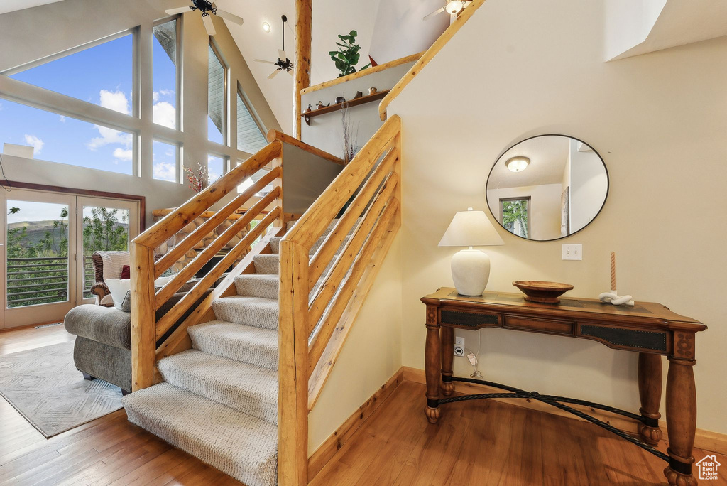 Staircase with wood-type flooring, a ceiling fan, a high ceiling, and baseboards