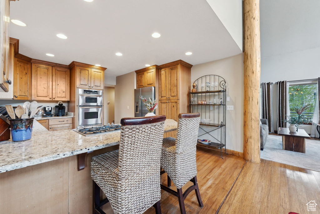 Kitchen with stainless steel appliances, light wood-style flooring, recessed lighting, a peninsula, and light stone countertops