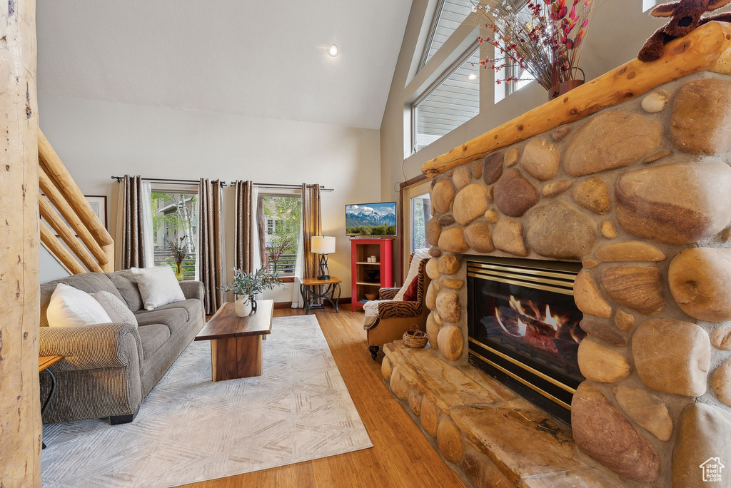 Living area with high vaulted ceiling, a stone fireplace, wood finished floors, and recessed lighting