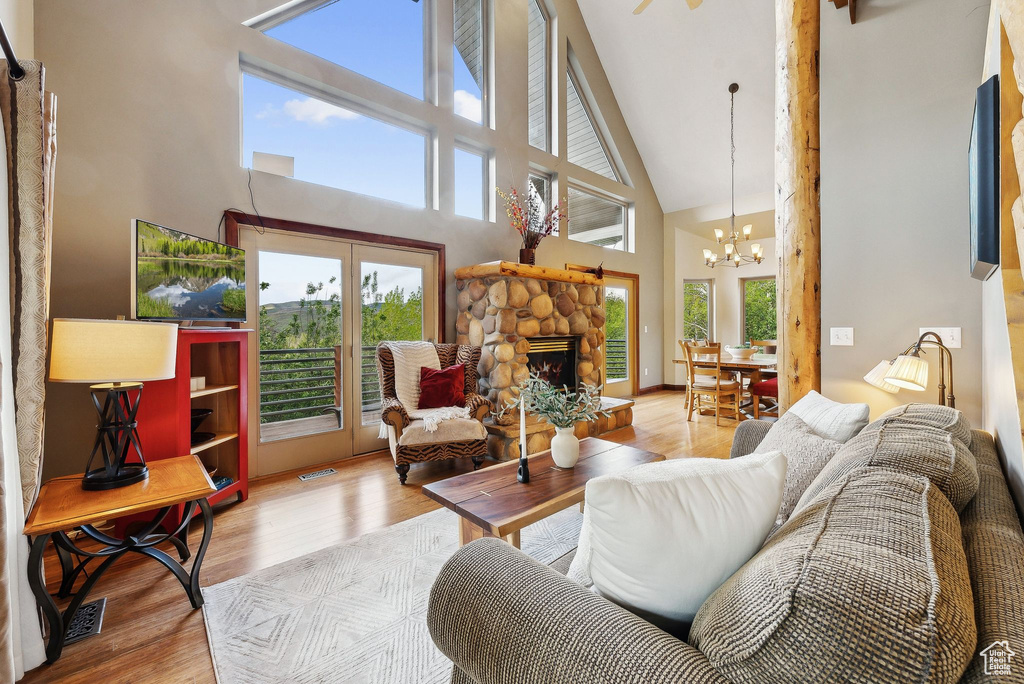 Living area featuring a high ceiling, wood finished floors, a chandelier, and a stone fireplace