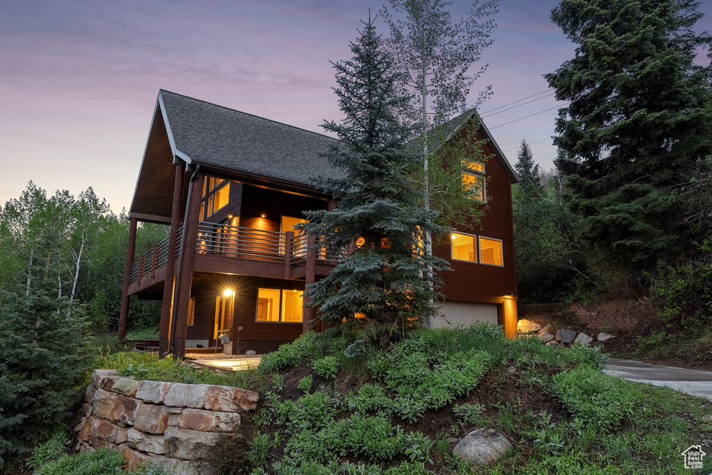 View of front of house featuring a garage, roof with shingles, and a balcony