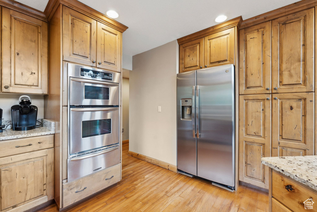 Kitchen featuring stainless steel appliances, a warming drawer, light wood-style floors, baseboards, and light stone countertops