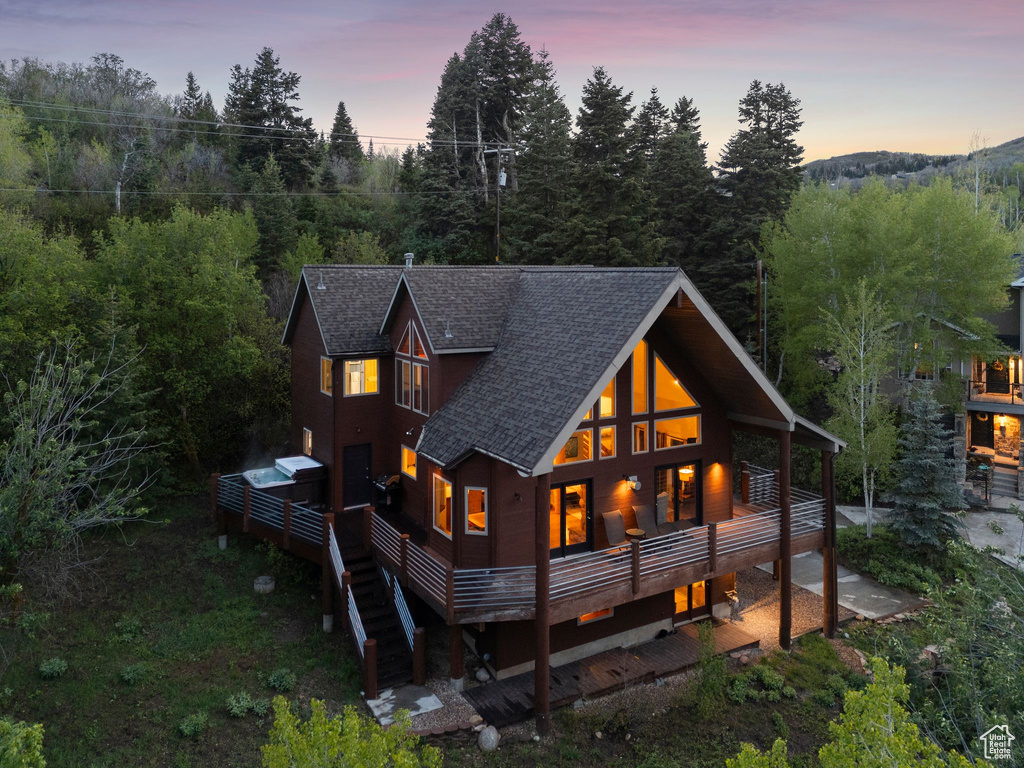 Back of house at dusk featuring a shingled roof and a deck