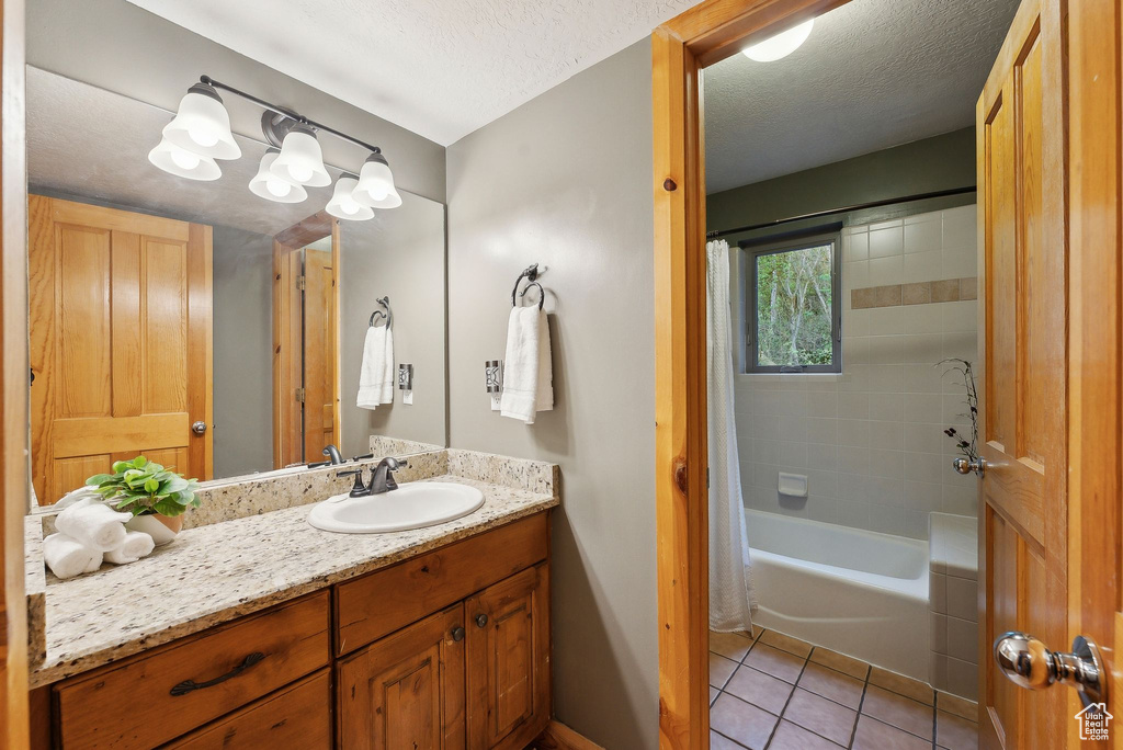 Full bath with tile patterned flooring, vanity, shower / bathtub combination with curtain, a textured ceiling, and baseboards