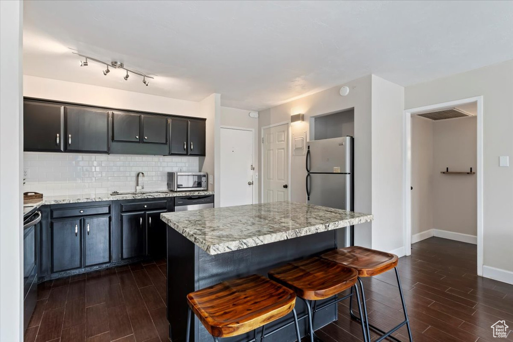 Kitchen featuring a sink, stainless steel appliances, dark wood-style floors, and a breakfast bar